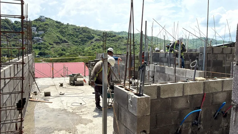 Foundation complete with workers placing concrete block walls on the first floor of Serena and the green hillside behind